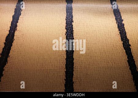Vertical black stripes on textured golden-brown surface. Pattern repeats evenly across material. Subtle sheen suggests natural fiber texture. Minimali Stock Photo