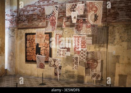Vintage textiles hang against weathered brick walls. Patterns in red and brown adorn delicate, handcrafted fabric. Art installation blends texture and Stock Photo