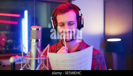 Thinking, man and musician with sheet in studio for songwriting, writing lyrics and recording audio. Male person, reflection and headphones with mic Stock Photo