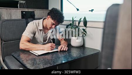Creative, journal and writing with man in RV for adventure hobby, road trip or travel information. Break, holiday and notebook with tourist person in Stock Photo