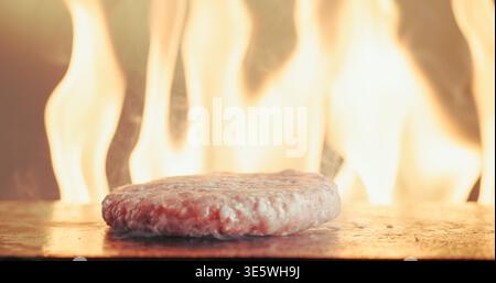 Grill, burger and patty in restaurant with fire, cuisine preparation or cooking meat for fast food. Flame, raw beef and protein in kitchen with steam Stock Photo