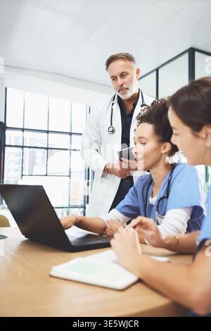 Doctor, laptop and training with students in hospital for healthcare internship or residency. Computer, medical coaching and review with people in Stock Photo