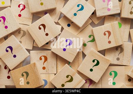 Too many wooden cubes with colorful question marks. Scattered blocks on blurred background symbolize curiosity and problem solving Stock Photo