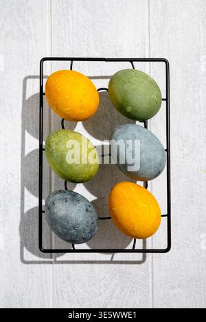 Easter eggs drying on a cooling rack after being naturally dyed with hibiscus and turmeric, creating a beautiful display of yellow and green hues, rea Stock Photo