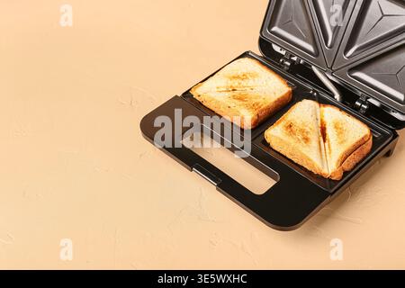 Modern sandwich maker with delicious grilled sandwiches on beige background Stock Photo