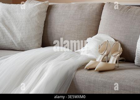 Stylish high heels with wedding dress on sofa in living room Stock Photo