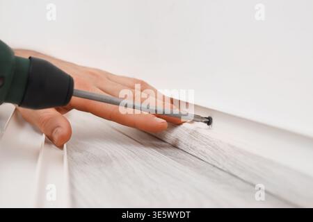 Worker with electric drill installing beautiful plinth on wall in stylish room, closeup Stock Photo