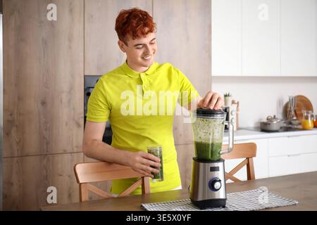 Young redhead man with glass of juice and blender in kitchen Stock Photo