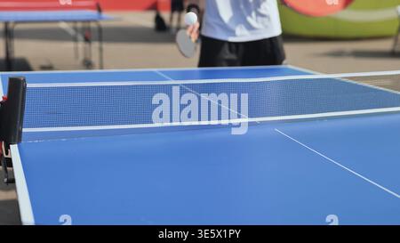 Adult playing table tennis outdoors, holding paddle hitting ping pong ball over net Stock Photo
