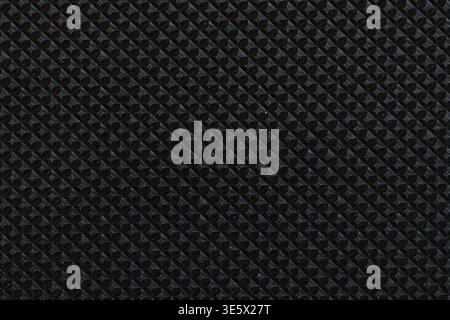 A close-up of a dark, textured surface featuring a repetitive diamond-patterned design with raised triangular facets, giving it a glossy yet rugged in Stock Photo