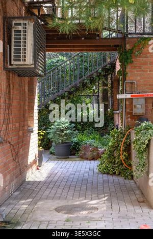 High-resolution photo of a narrow alleyway flanked by rustic brick buildings in Tbilisi, Georgia. The charming scene features textured walls, soft sun Stock Photo