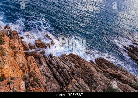 the sea breaking on the reddish rocky coast Stock Photo
