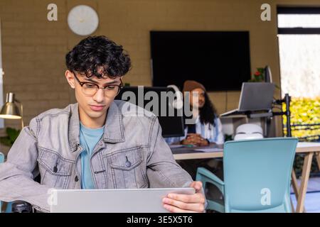Diverse male coworkers working in shared workspace, Asian man using laptop, colleague using monitor Stock Photo