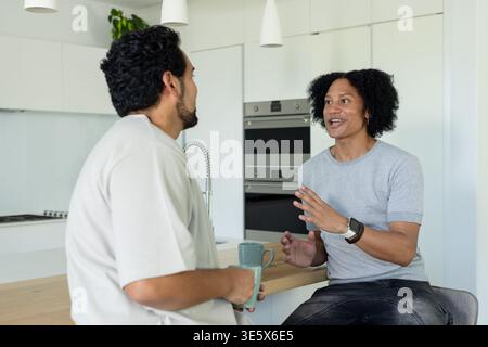 African American men chatting at modern kitchen island on wooden countertop, holding ceramic mugs Stock Photo