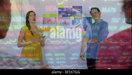 Showing woman in yellow with marker, man in blue pointing at wall, sticky-notes, tickers-on-glass Stock Photo