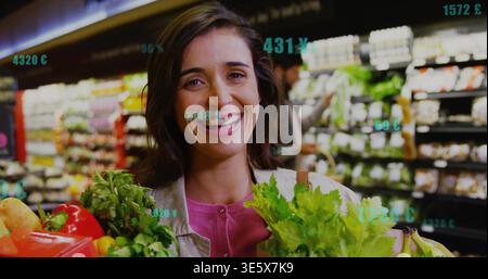 Smiling woman in pink top holding leafy greens and red pepper in market, with green overlays Stock Photo