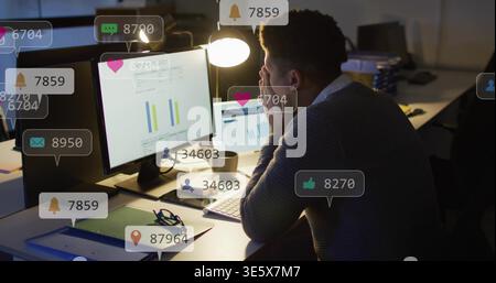 Analyzing charts, man in dark sweater viewing dual monitors at desk, laptop, alerts, copy space Stock Photo