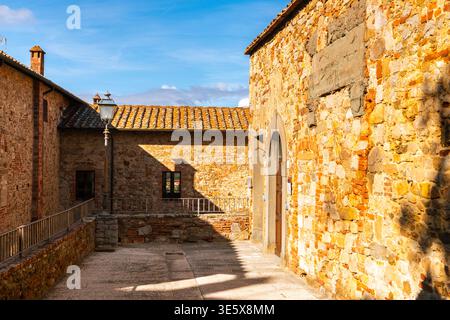 Lucignano, Italy, a charming alleyway in Piazza del Tribunale, Tuscany, presenting historic brick and stone architecture with warm afternoon light, It Stock Photo