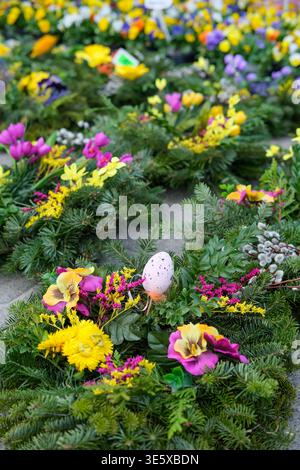 Rows of Easter wreaths decorated with colorful flowers and egg ornaments are displayed for sale at an outdoor flower market Stock Photo