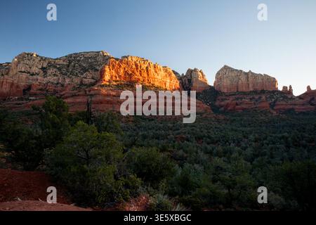 Warm sunset light glowing on red rock cliffs above desert forest Stock Photo