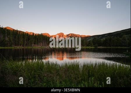 Sprague Lake reflecting sunlit mountains and pine trees at dawn Stock Photo