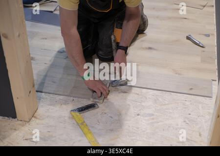 Worker installing laminate flooring by hand with hammer and measuring tape during home renovation project Stock Photo