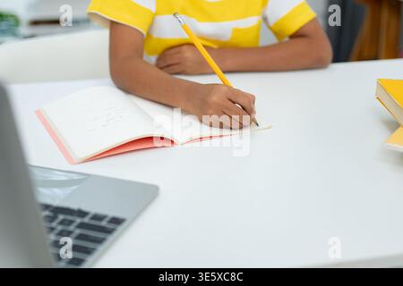 Child Writing Notes in Notebook with Laptop on Desk Online Learning Stock Photo