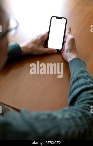 Over the shoulder of elderly man using smartphone with glowing screen Stock Photo