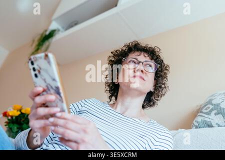 White woman in her 40s looking at smartphone with thoughtful expression Stock Photo