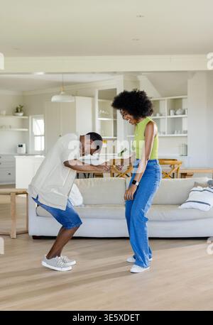 African American couple dancing playfully in bright living room with sofa, coffee table, smartwatch Stock Photo