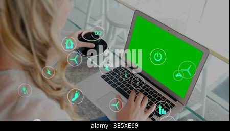 Working woman wearing blouse typing on laptop with power icon at glass-top table, holding black cup Stock Photo
