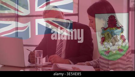 Discussing suited man and striped-top woman reviewing papers at table, with laptop and flag overlay Stock Photo