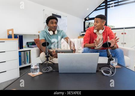 Recording Diverse male friends using two microphones on couch in loft studio, with silver laptop Stock Photo
