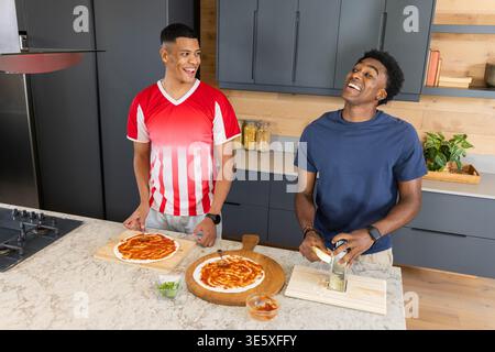 Preparing pizza on marble counter in kitchen by diverse male friends, using pizza peels and grater Stock Photo