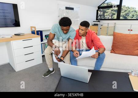 Discussing project ideas Diverse male coworkers sitting in office lounge, with laptop and documents Stock Photo