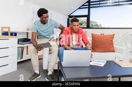 Diverse male friends working on laptop and tablet in loft living room, with papers, coffee table Stock Photo