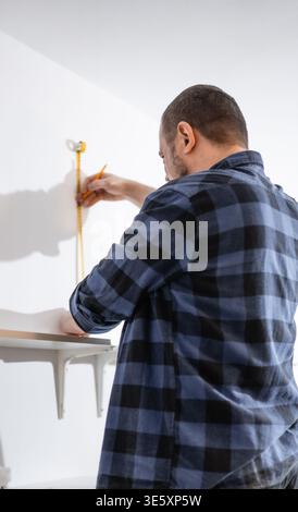 Handyman making marks on the wall for bookshelf mounting, person doing home renovation and furniture assembly by himself, DIY concept of house Stock Photo