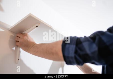 Handyman mounting shelf brackets, professional furniture assembly and wall decoration concept. Stock Photo