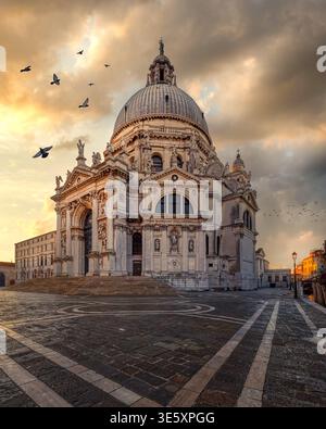 Basilica di Santa Maria della Salute under dramatic golden clouds with birds flying above the square, Venice, Italy. Stock Photo
