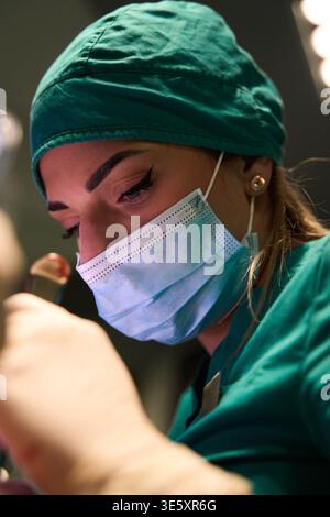 Female surgeon focused during delicate surgery in an operating room wearing mask and scrubs Stock Photo