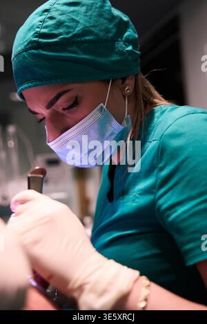 Female surgeon focused during surgery in operating room wearing mask and surgical scrubs Stock Photo