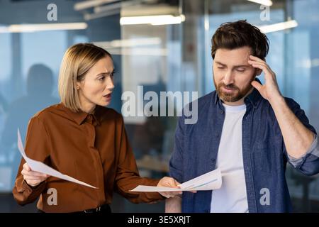 Female manager feeling frustrated while scolding her male employee for poor work results, triggering emotions of stress, conflict, and pressure in a modern office environment Stock Photo