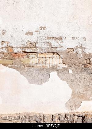 Peeling White Painted Wall with Exposed Old Bricks in Sunlight Stock Photo