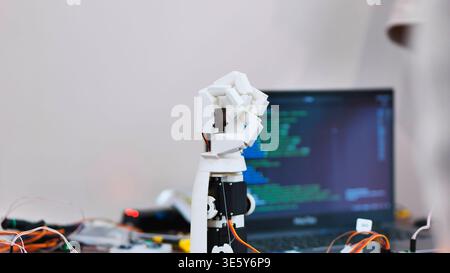 A robotic arm prototype on a desk with a laptop showing programming code in the background Stock Photo