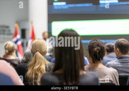 Rear view of business professionals attending corporate conference, listening to keynote speaker with presentation screen and national flags in modern Stock Photo