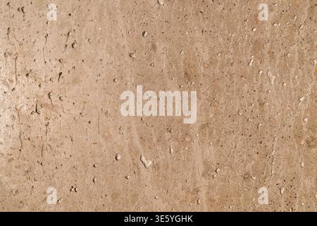 Closeup of beige travertine stone wall showing porous, pitted surface with natural grain and subtle color variations across vertical slab. Stock Photo