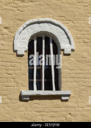 Ancient arched window with bars on yellow brick wall of old building. Close-up. Copy space Stock Photo