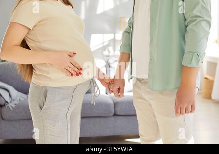 Happy young couple standing together at home, holding hands, supporting each other during pregnancy. Stock Photo