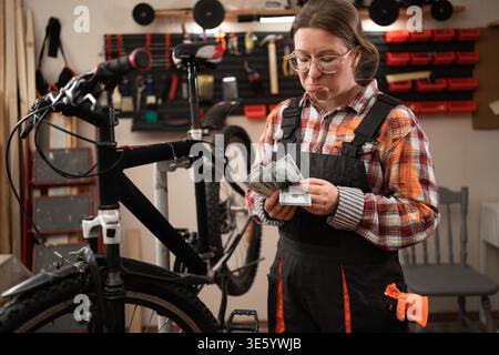Female bike repairman repairing mountain bicycle with equipment for mechanic or technician writing notes in workshop. Bicycle repair, maintenance and Stock Photo