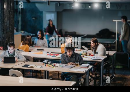 Students studying together in a shared coworking space with books and laptops Stock Photo